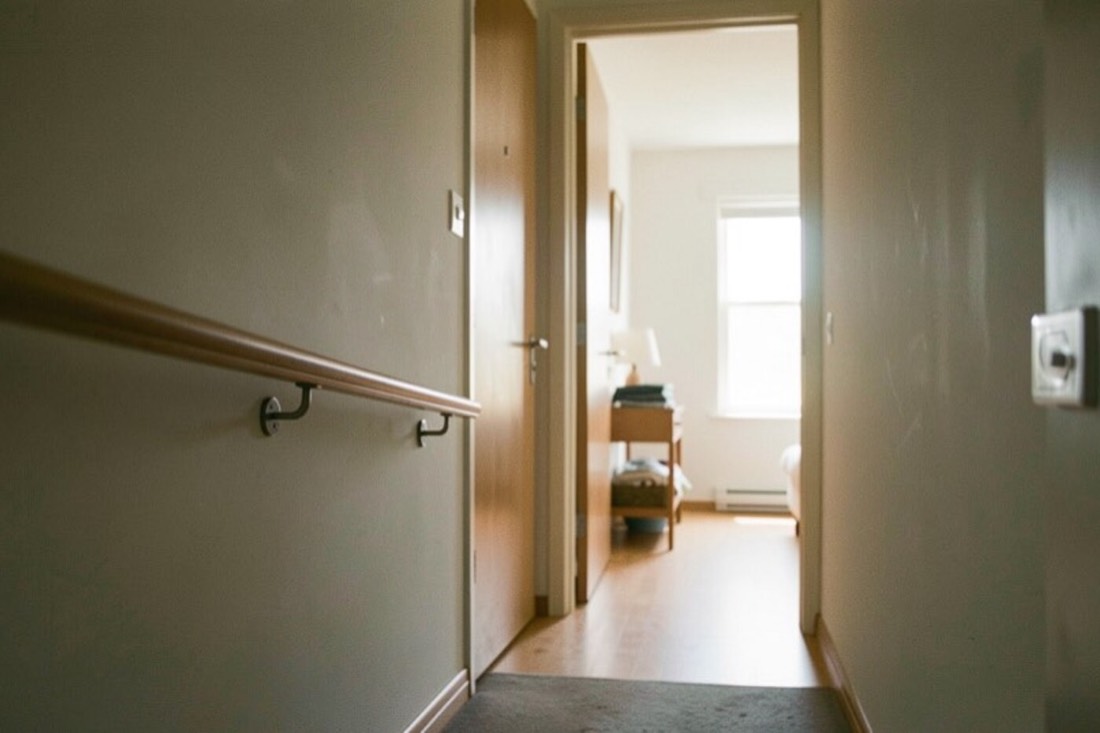 Un passage intérieur sans ressaut relie un seuil d'entrée à une pièce éclairée, avec une main courante discrète